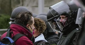 Ein Demonstrant mit Mund-Nasen-Schutz steht einem behelmten Polizisten gegenüber.
